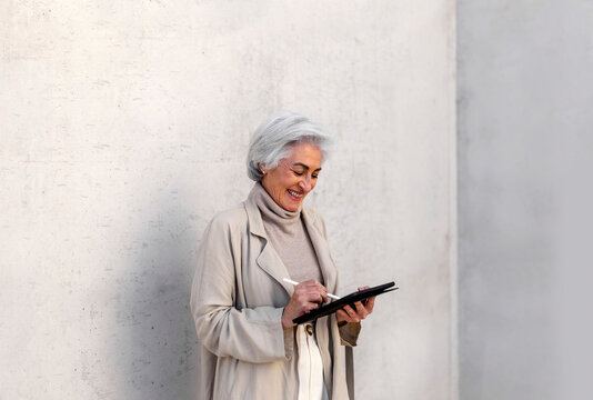 Happy woman using digital tablet in front of wall