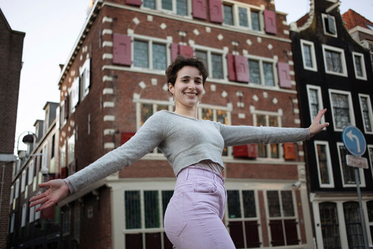 Happy young woman with arms outstretched dancing in front of building