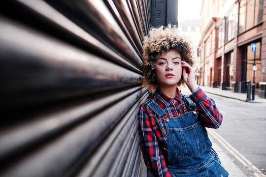 Young woman with hand in hair leaning on corrugated iron
