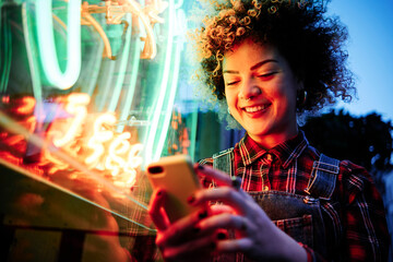 Smiling woman using mobile phone by neon lights at Chinatown