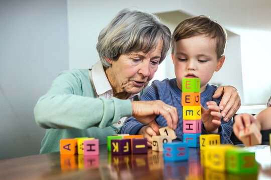 Grandmother helping grandson stacking toy blocks at home