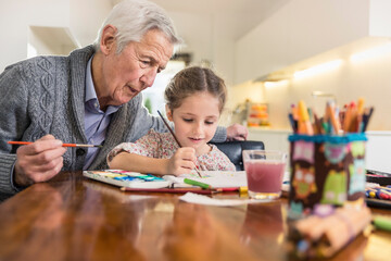 Granddaughter and grandfather painting together at home
