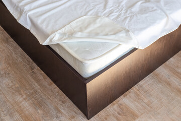 Corner of a wooden bed with a high mattress and a protective cover. Putting on the mattress topper