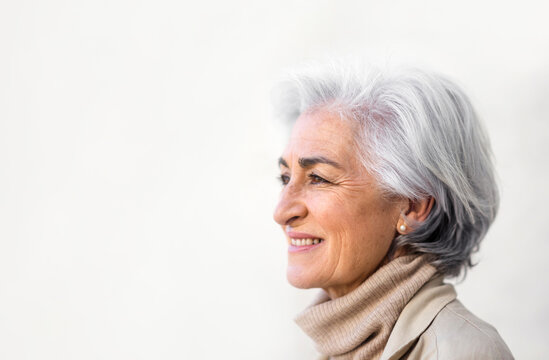 Smiling woman with gray hair contemplating by white wall