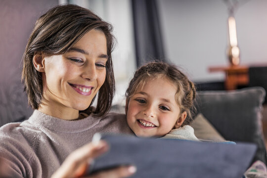 Smiling mother and daughter using digital tablet at home