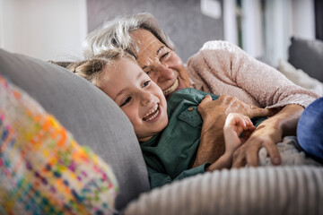 Happy grandmother and granddaughter resting on sofa in living room