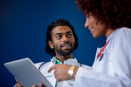 Male and female doctors discussing over digital tablet against blue background