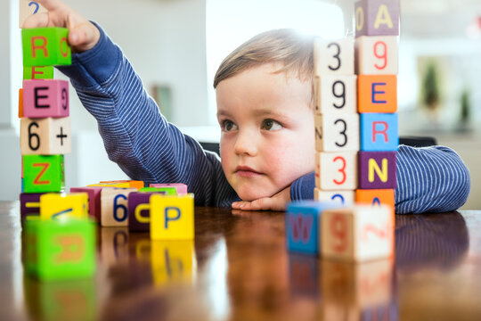 Cute boy playing with toy blocks on table at home