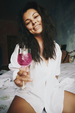Hispanic woman with wineglass sitting in bedroom