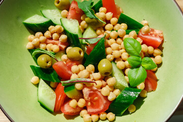 Vegetable salad of cucumbers and tomatoes with chickpeas in a green plate