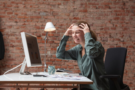 Stressed female entrepreneur with hands in hair sitting at desk in office