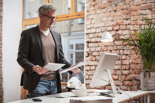 Mature man with digital tablet and paper document working in office