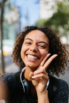 Cheerful woman showing peace sign in city
