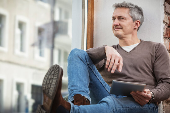 Caucasian man with digital tablet looking through window while sitting at home
