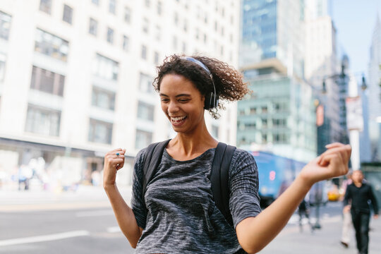 Cheerful woman dancing while listening music through headphones in city