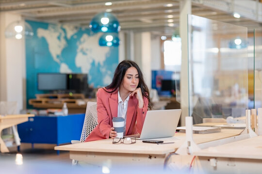 Female professional with hand on chin looking at laptop at desk