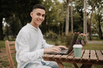 Fototapeta premium Young handsome freelancer working on laptop remotely. Happy man in a IT park, doing his work from distance.