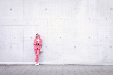 Woman in smart casual using mobile phone in front of concrete wall