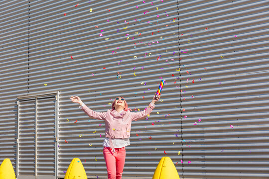 Happy woman with party popper enjoying confetti during sunny day