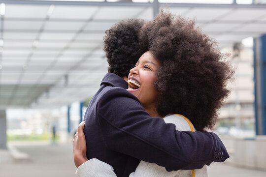 Laughing Afro woman embracing boyfriend at railroad station