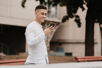 Young handsome model with a cellphone. Man smiling outside.