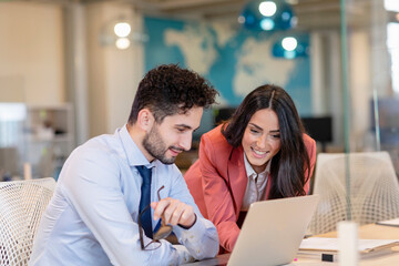Smiling male and female professionals discussing over laptop in coworking office