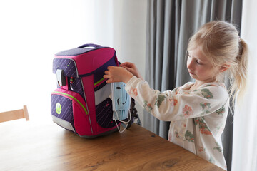 Girl tying face mask on backpack at home