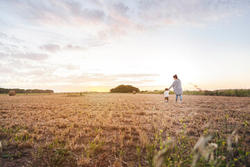 Mother walking with baby son through harvested field at sunset