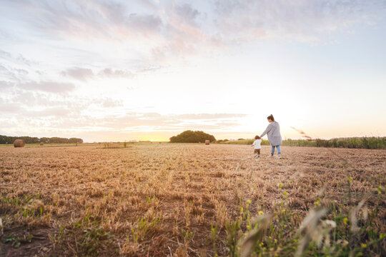 Mother walking with baby son through harvested field at sunset