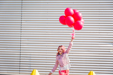Woman with arms raised holding helium balloons in front of corrugated wall