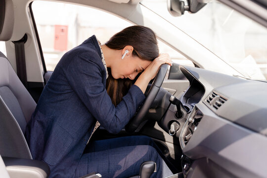 Tired businesswoman resting head on steering wheel in car