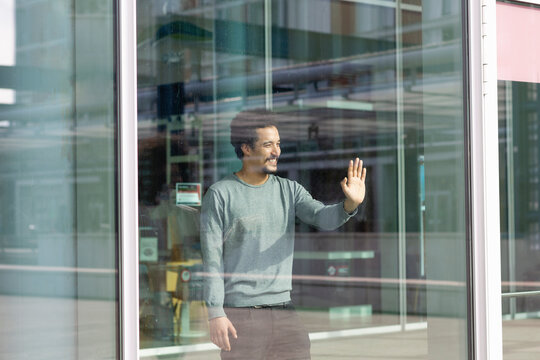 Smiling man looking away while touching glass wall