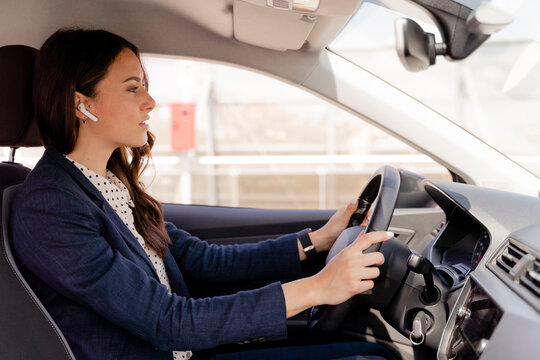 Businesswoman driving car while wearing in-ear headphones