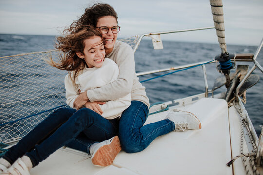 Cheerful mother embracing daughter while traveling on sailboat