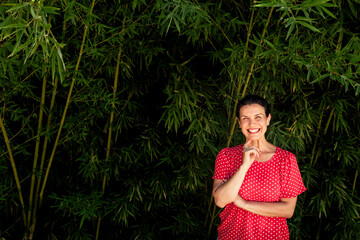 Cheerful woman with hand on chin standing in front of bamboo plants