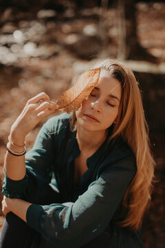 Woman touching dry leaf on face during autumn