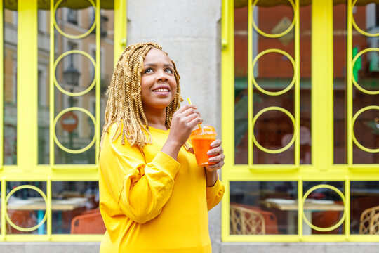 Smiling woman holding juice while looking up and day dreaming