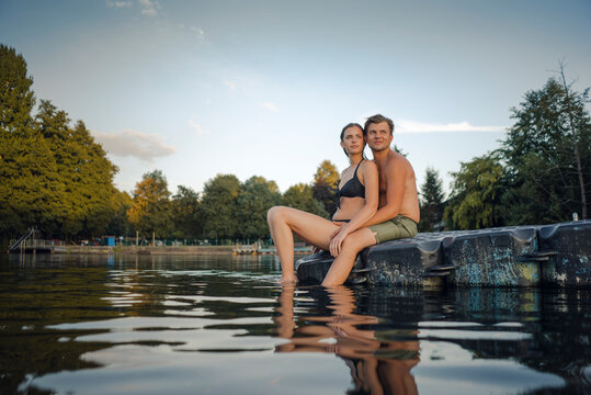 Young couple sitting on bathing platform on a lake looking at distance