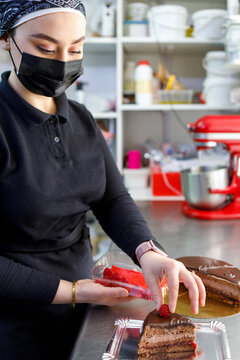 Female baker placing raspberry on cake slice at bakery