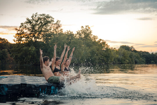 Friends having fun at the lake, sitting on bathing platform, slpashing water