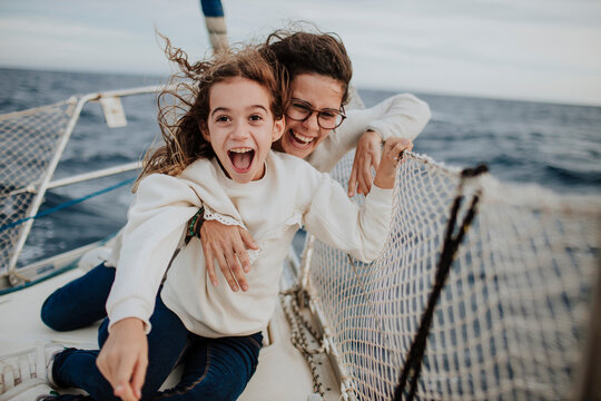 Laughing mother with excited daughter on sailboat during vacation