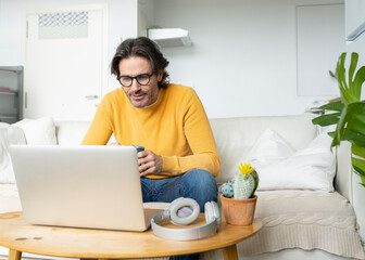 Man with eyeglasses looking at laptop while sitting on sofa in living room