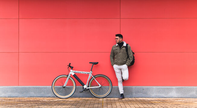 Young businessman by bicycle leaning on red wall