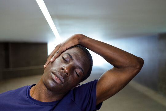 African man with eyes closed standing in underground stretching neck