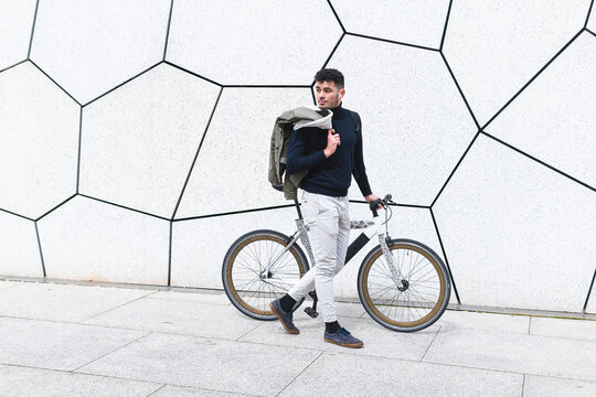Young man looking away while walking with bicycle on footpath
