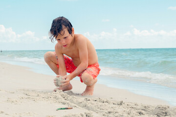 Child play on a tropical beach. Kid playing in the sea on summer family vacation. Children have fun at the beach resort. Funny boy writes on the sand.Active children's lifestyle, swimming people