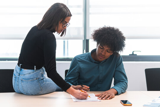 Female business professional assisting male colleague while working on document at desk