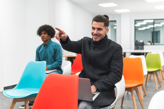 Smiling businessman gesturing while sitting by coworker in classroom