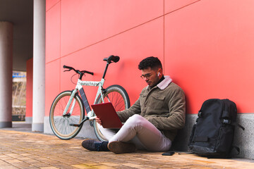 Male entrepreneur using laptop while sitting by bicycle on footpath