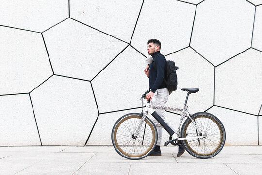 Young man wheeling bicycle by textured white wall